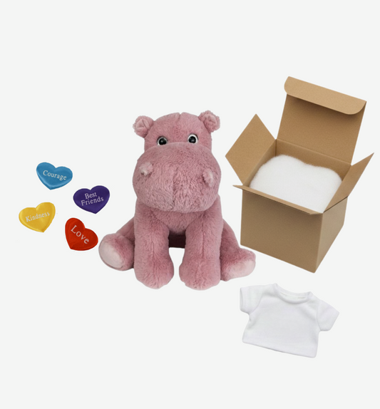 Pink plush hippo toy with a cardboard box, colorful heart-shaped tags, and a white shirt on a white background.